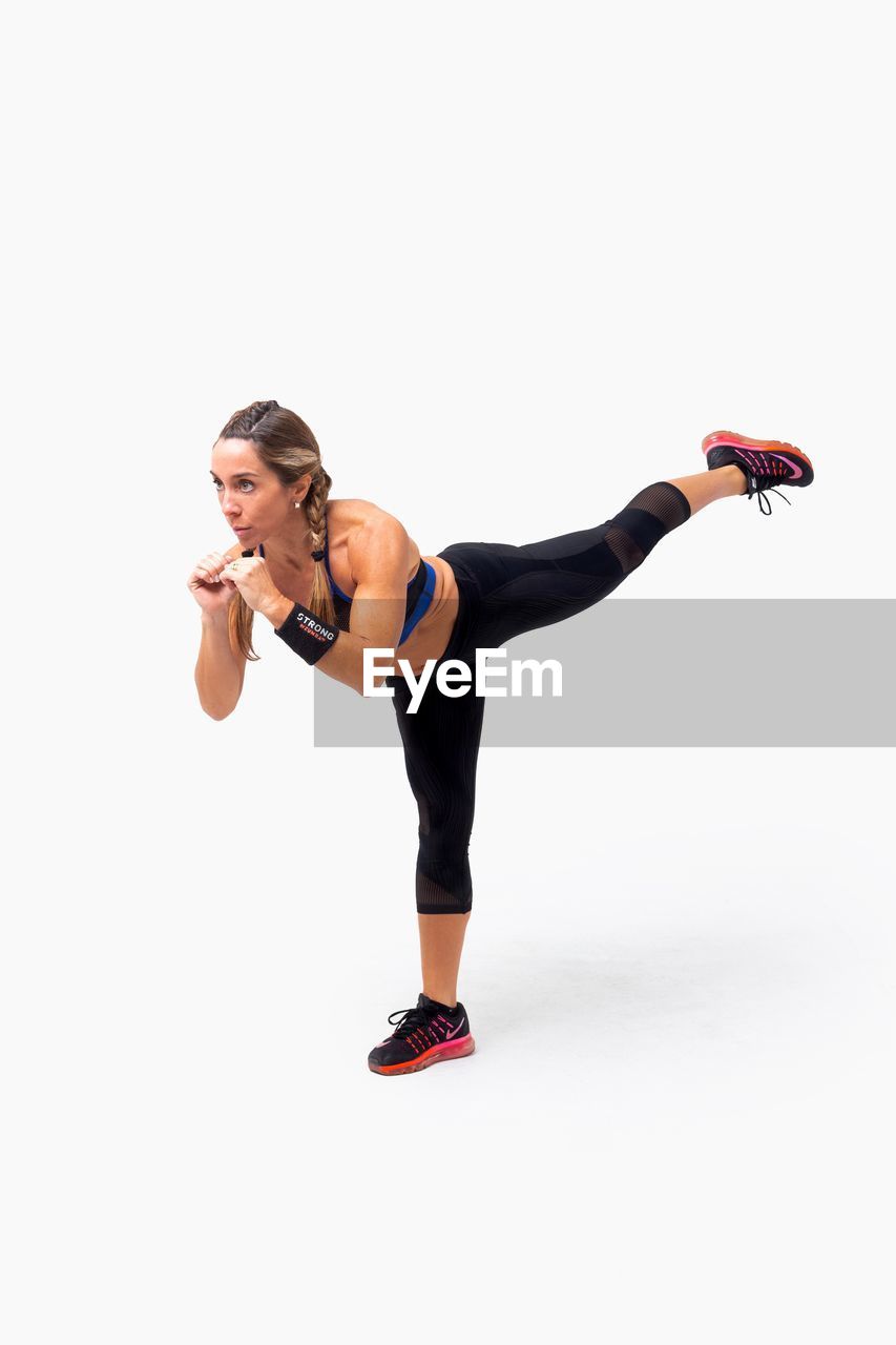 Woman exercising while standing against white background