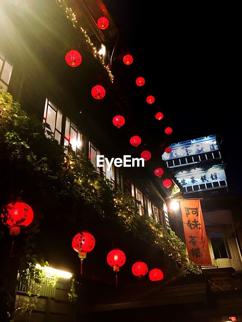 LOW ANGLE VIEW OF ILLUMINATED LANTERNS HANGING IN CITY