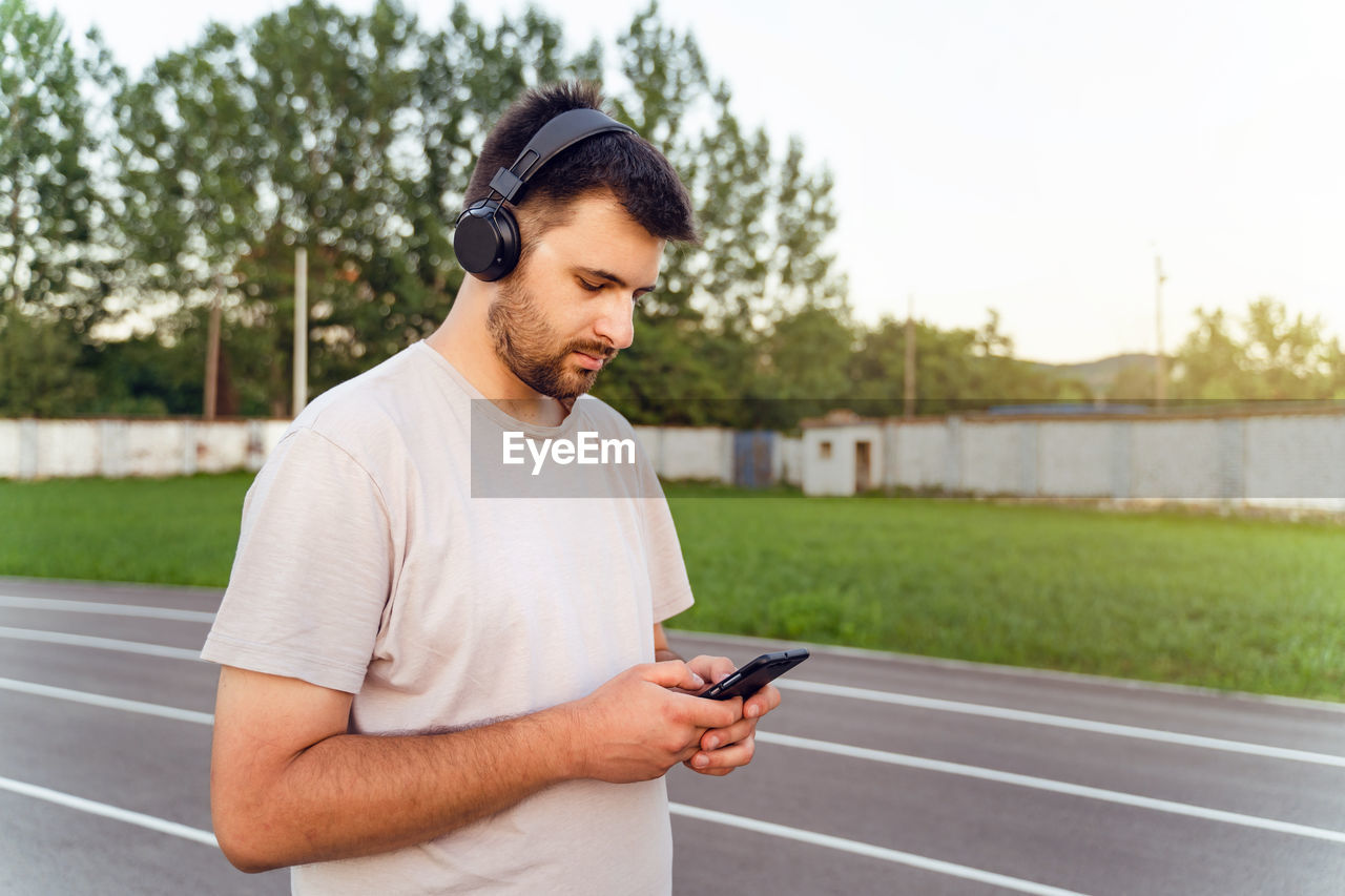 YOUNG MAN USING MOBILE PHONE WHILE STANDING ON CAMERA LOOKING AT SMART