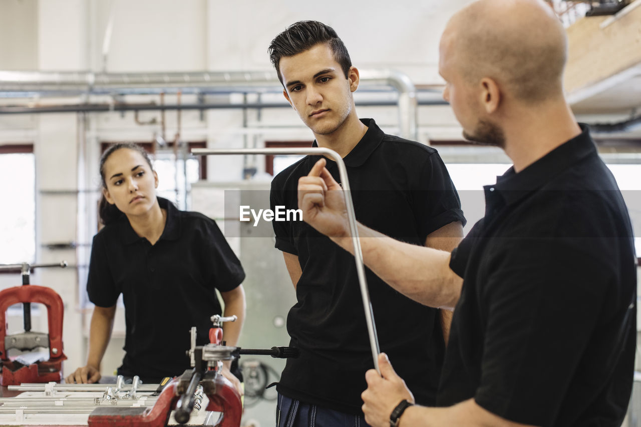 Auto mechanic teacher explaining metallic rod to students in training class