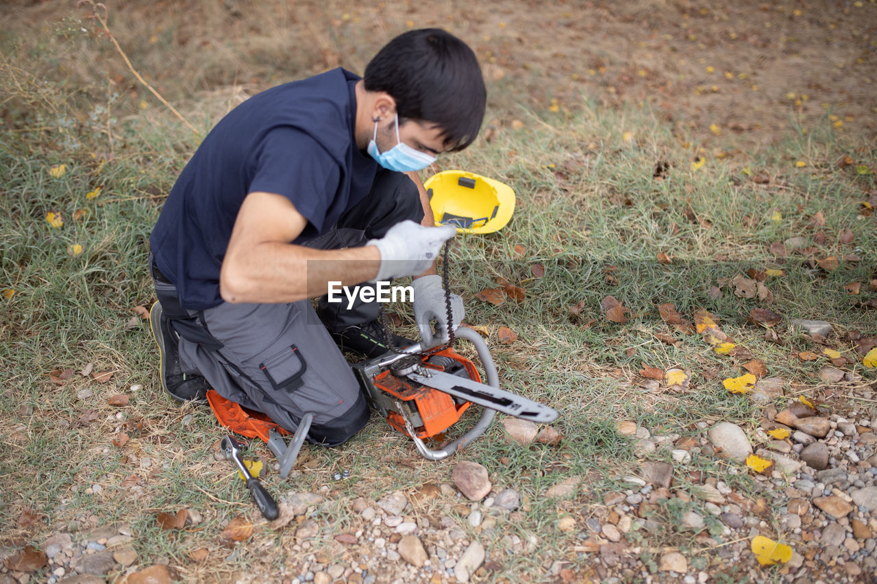 High angle view of man wearing mask holding chainsaw on field