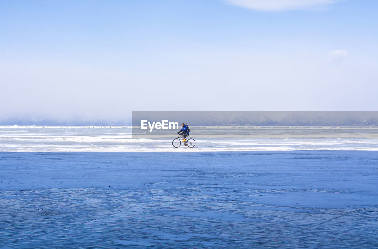 Man riding bicycle on snow covered land against sky