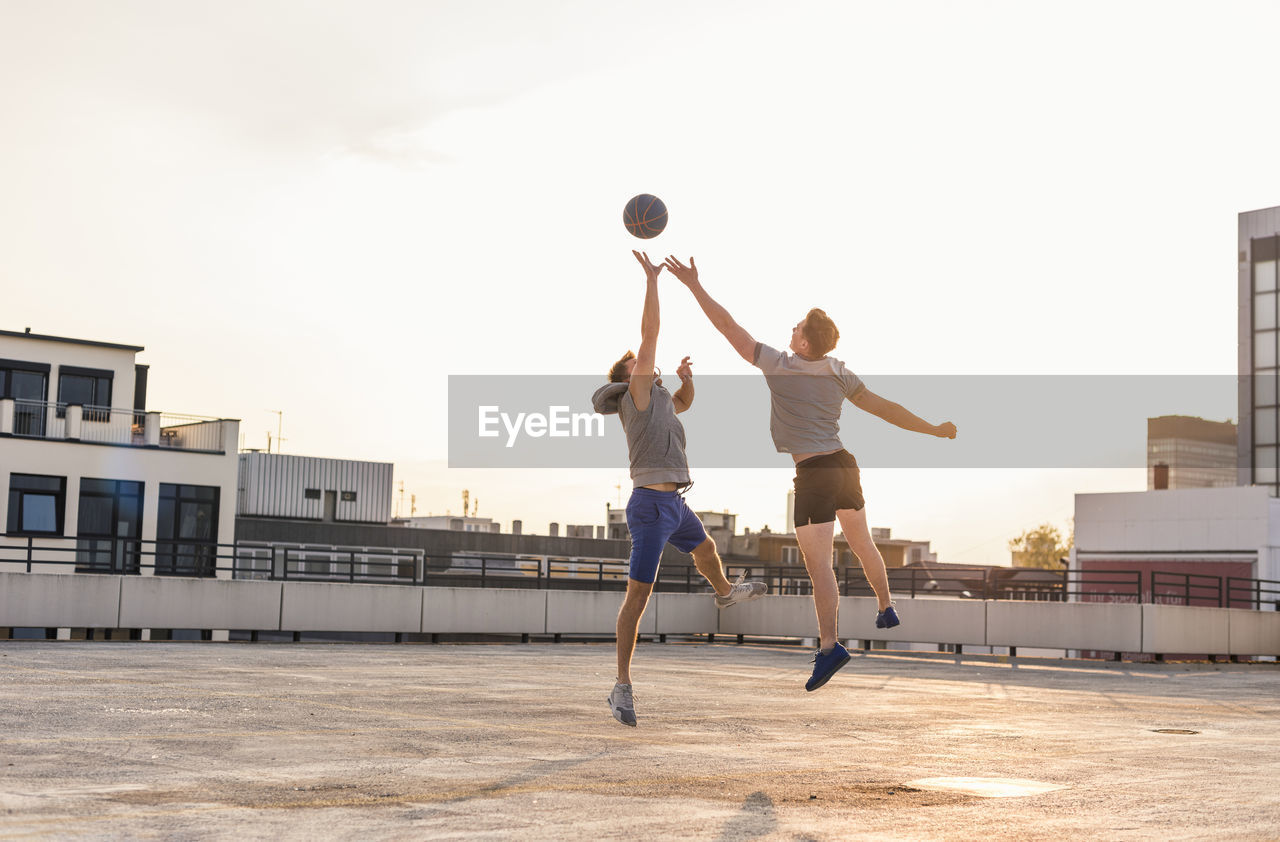 Friends playing basketball at sunset on a rooftop
