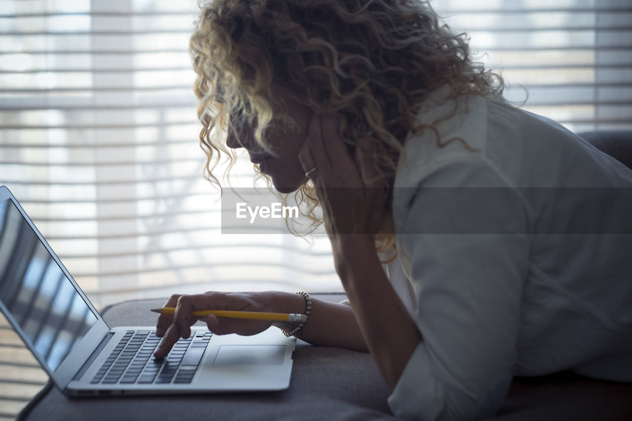 SIDE VIEW OF SENIOR WOMAN USING LAPTOP