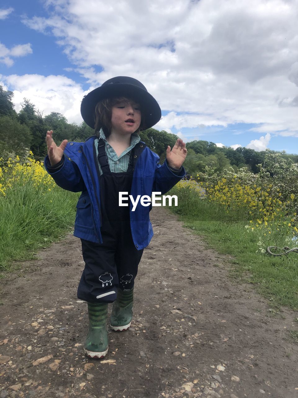 Boy with hat standing on path against sky