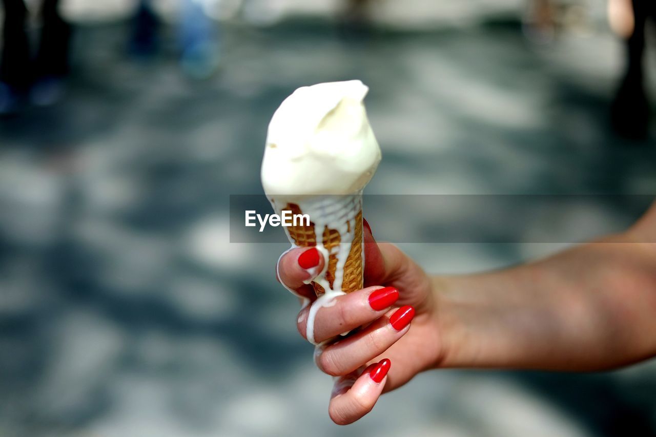 Cropped image of woman holding meting ice cream cone outdoors