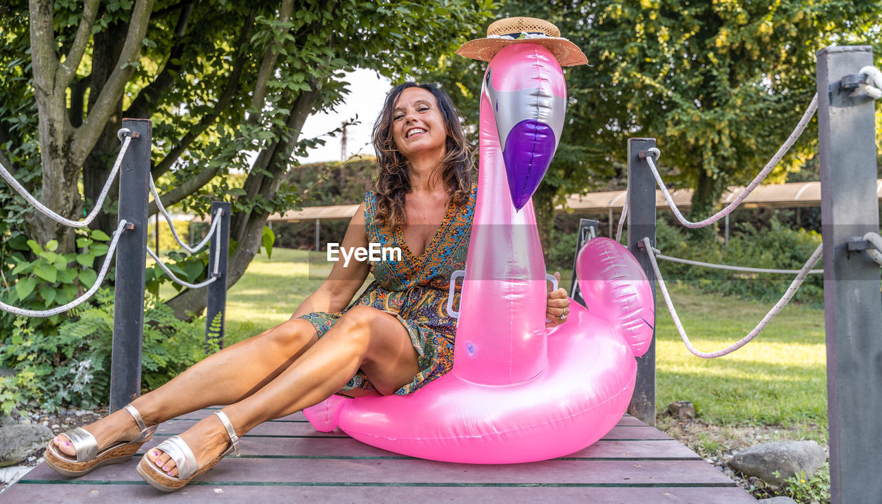 Portrait of beautiful middle aged woman sitting on pink flamingo inflatable toy