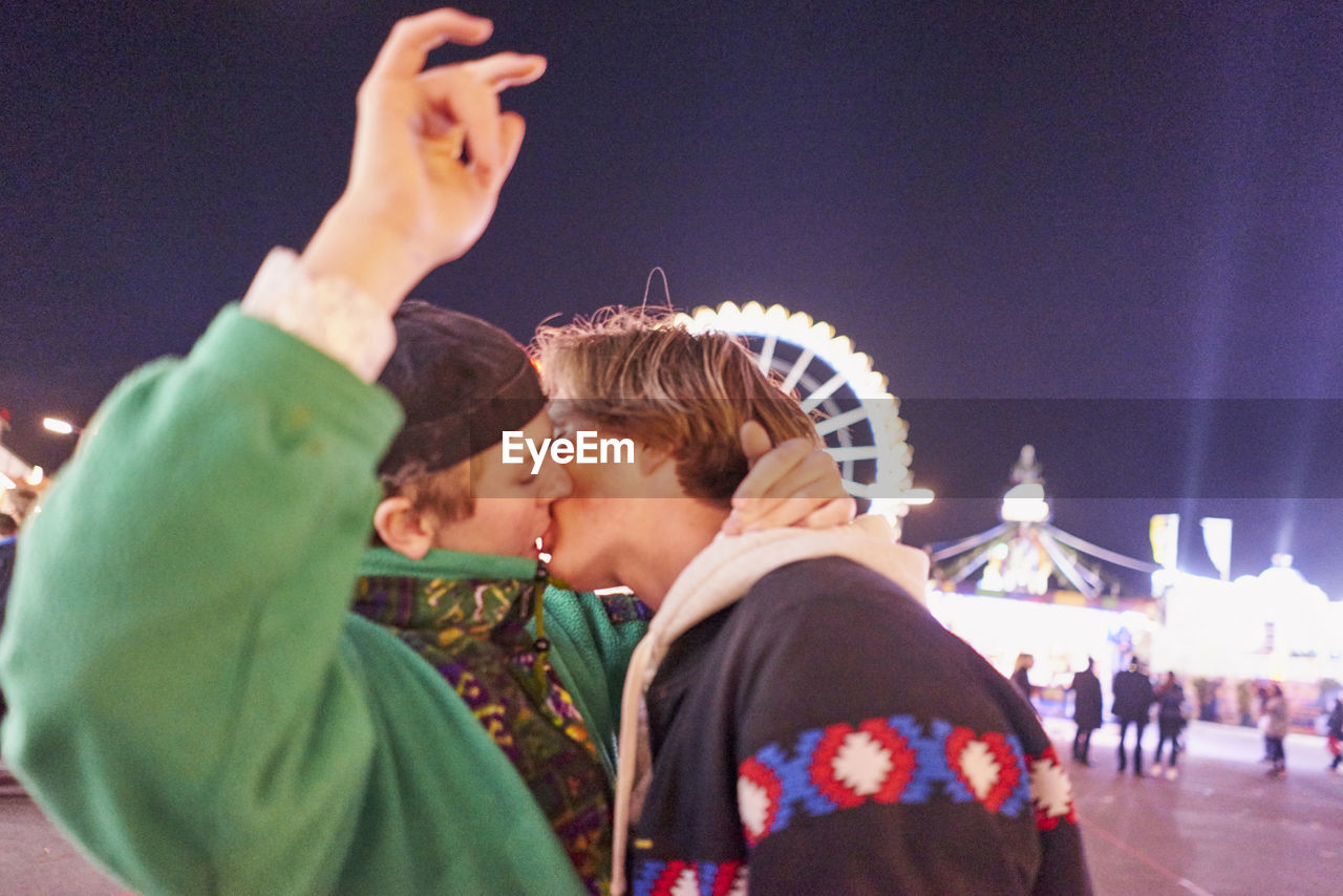 Gay men kissing at amusement park during night