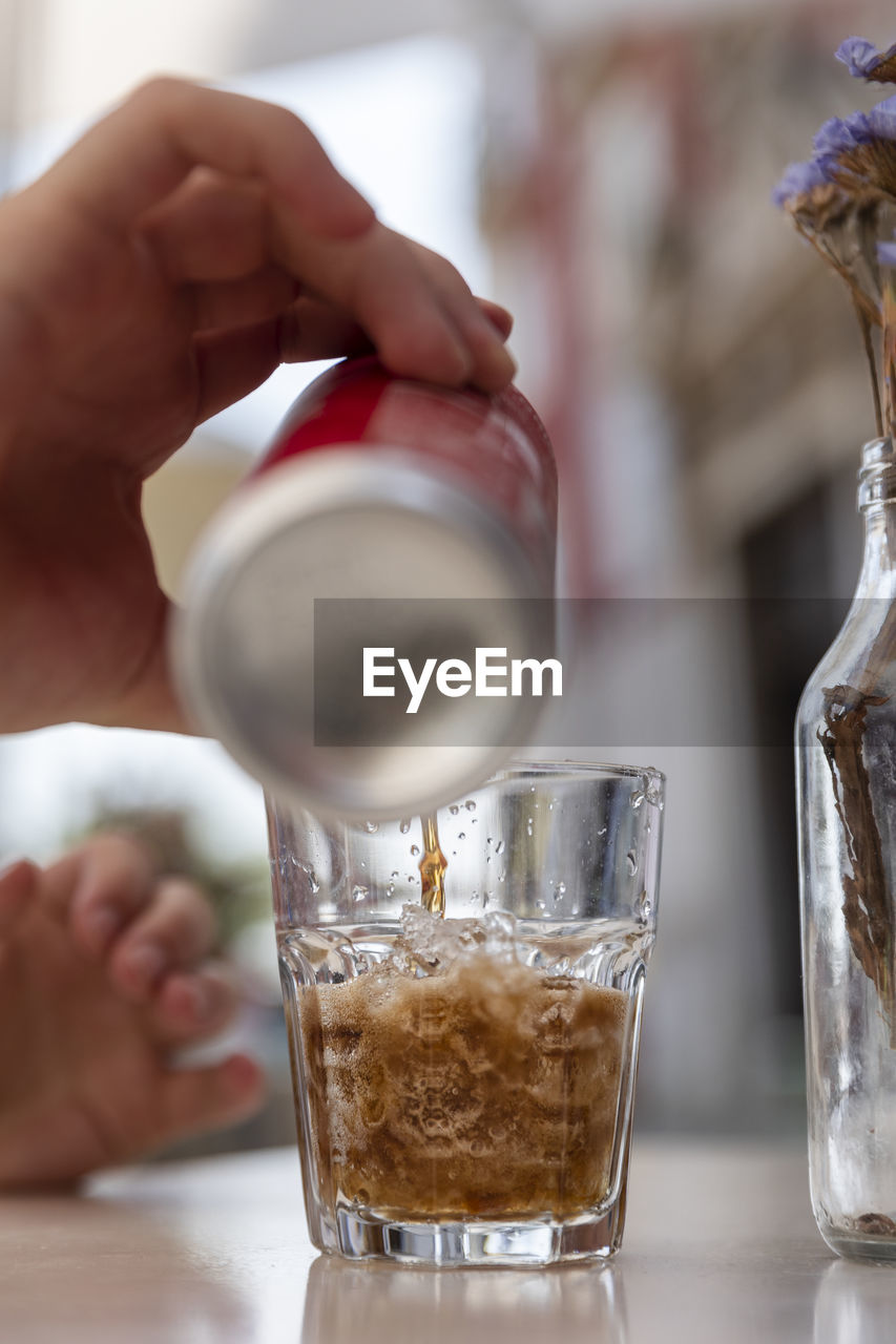 Human hand pours chilled soft drink into glass with ice cubes