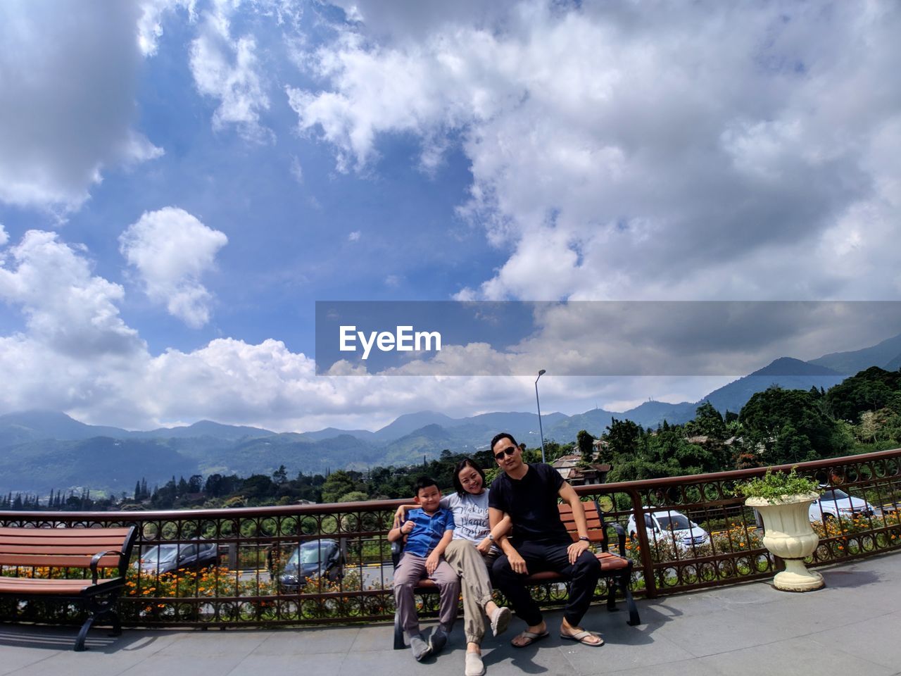 PEOPLE SITTING ON RAILING AGAINST MOUNTAINS