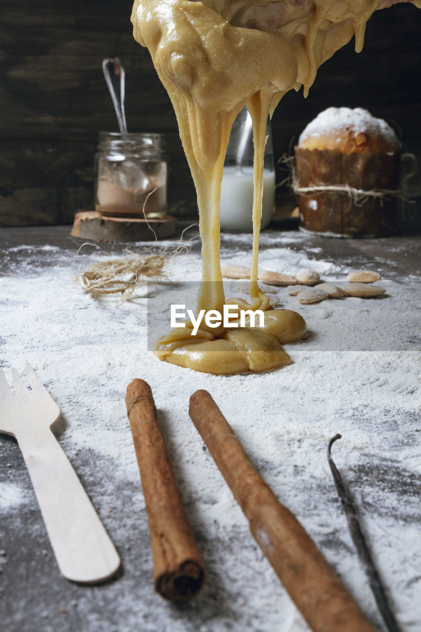 Spicy yellow dough for traditional christmas panettone cake falling on table sprinkled with flour with cinnamon and vanilla and ready baked cake in background