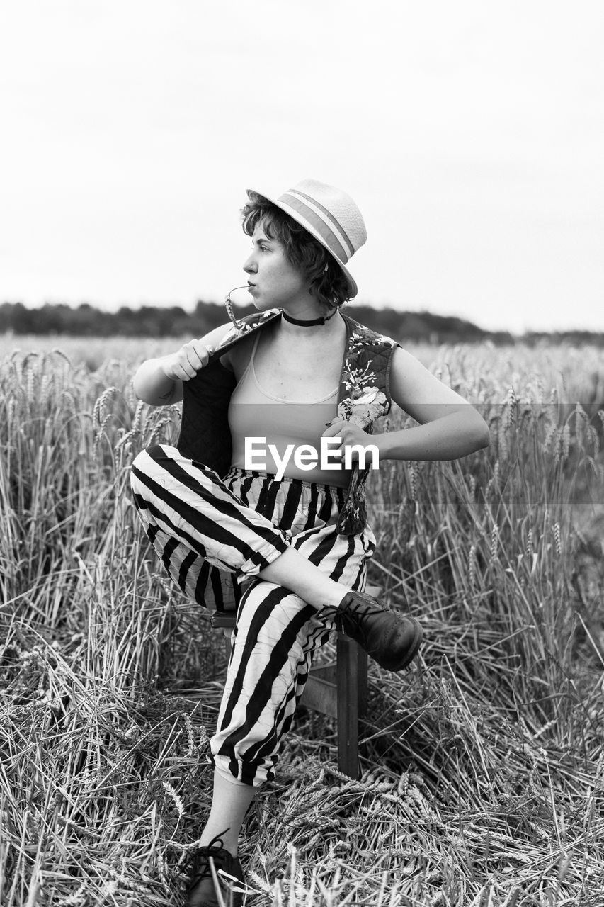 Full length of woman looking away while sitting on field against sky