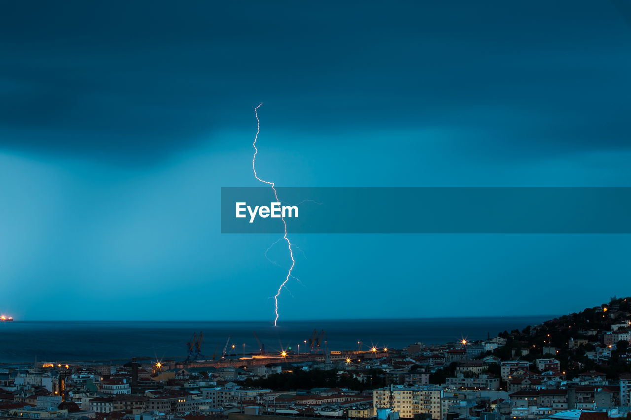 Lightning over sea by city at dusk