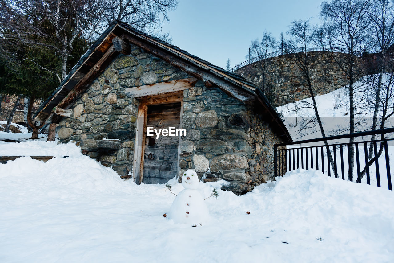 SNOW COVERED HOUSE BY TREES AGAINST SKY