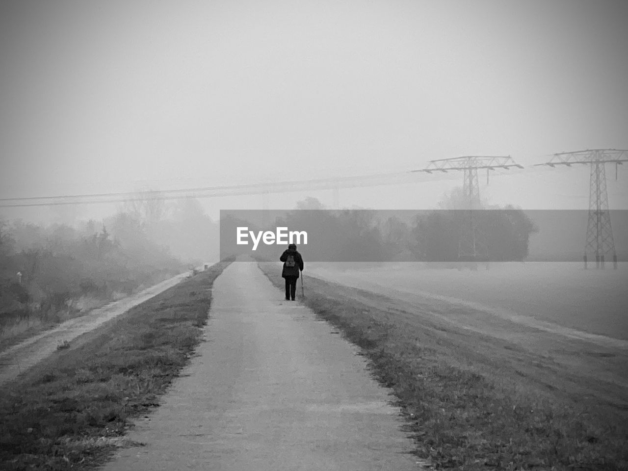 REAR VIEW OF MAN WALKING ON ROAD IN FOGGY WEATHER