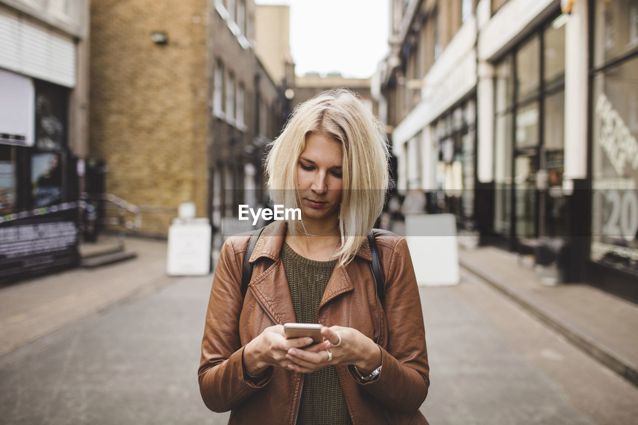 Young woman using mobile phone on road in city