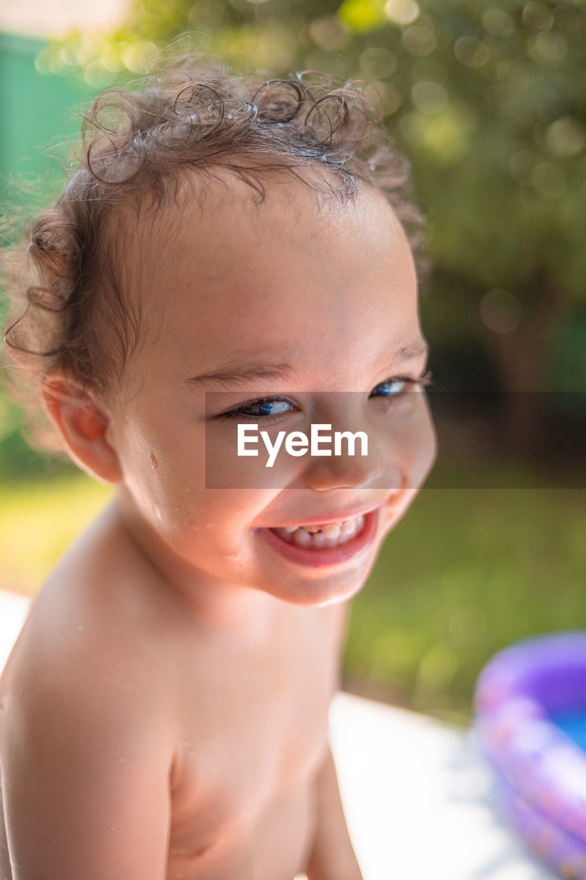 Happy kid playing in an inflatable pool in backyard. curly toddler smiling and playing with water