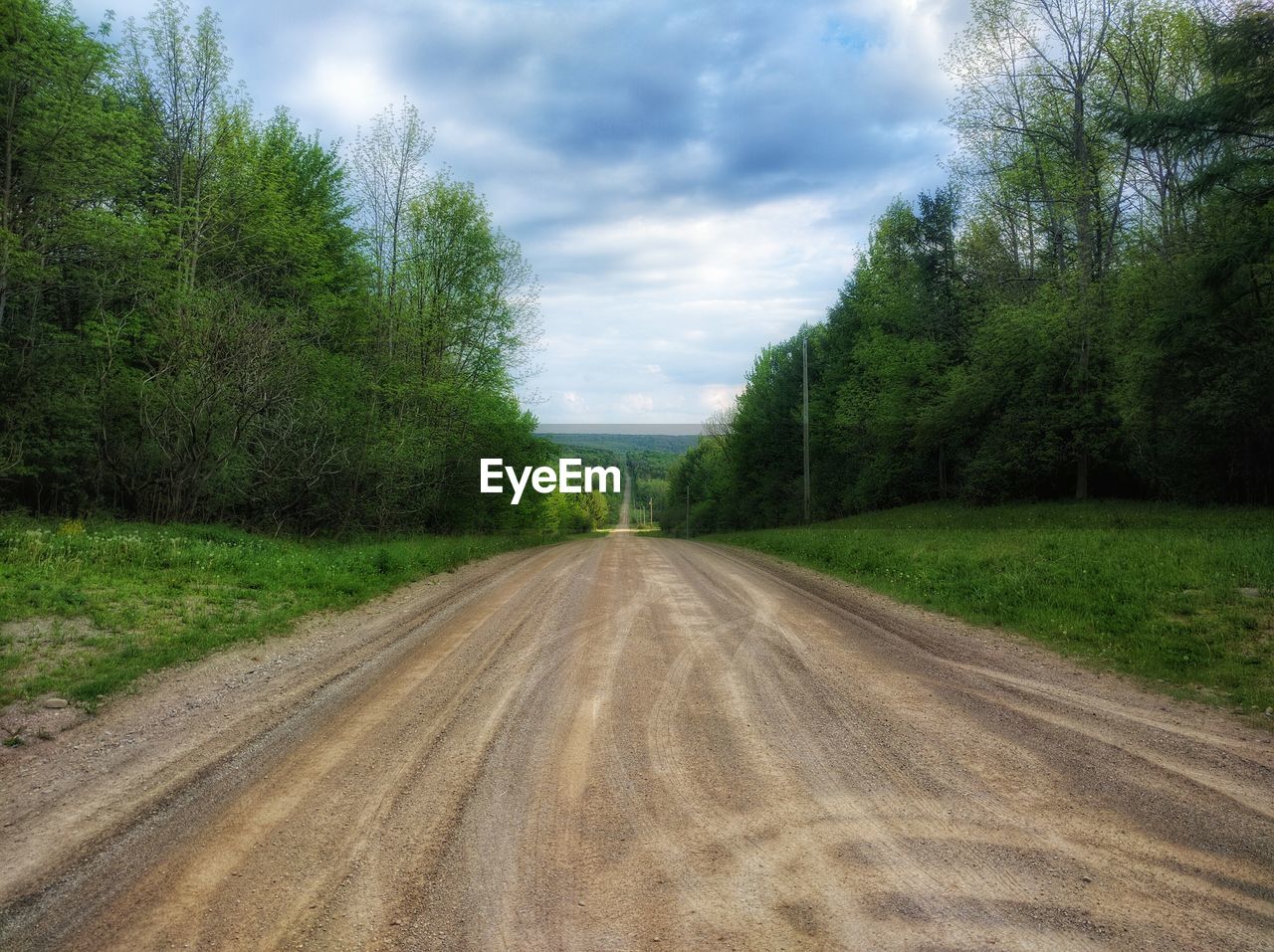 ROAD PASSING THROUGH FIELD AGAINST CLOUDY SKY