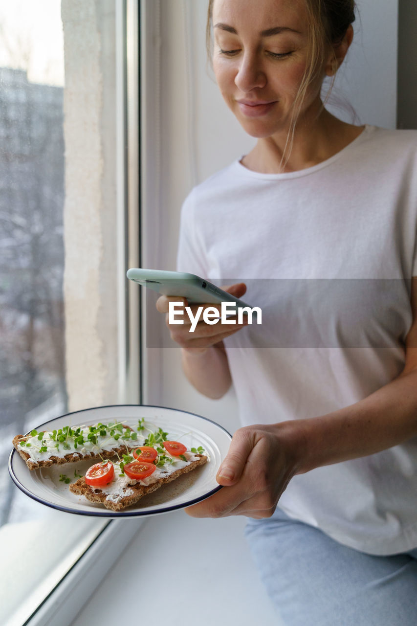 Woman photographing food in plate with mobile phone at home