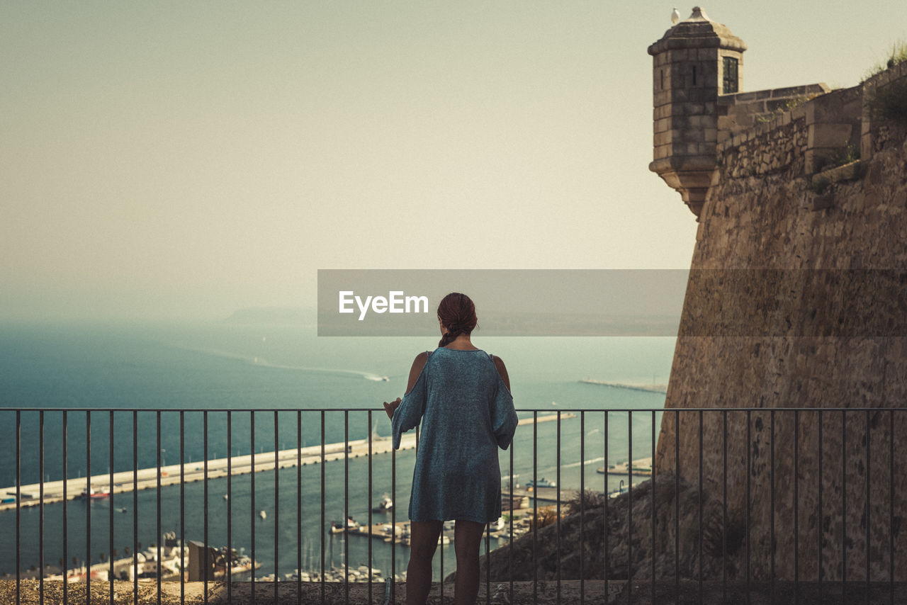 Rear view of woman standing by railing against sea