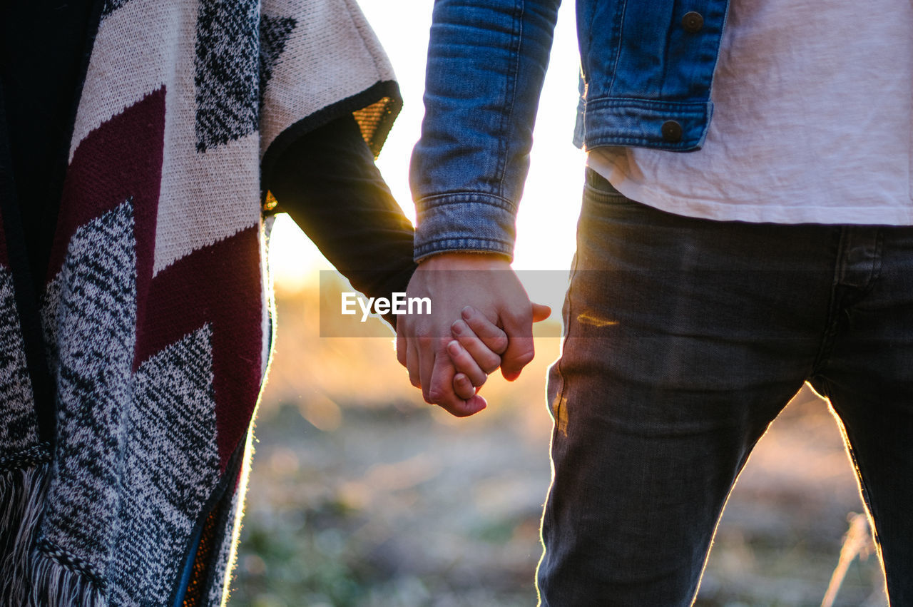 Cropped image of couple holding hands on sunny day