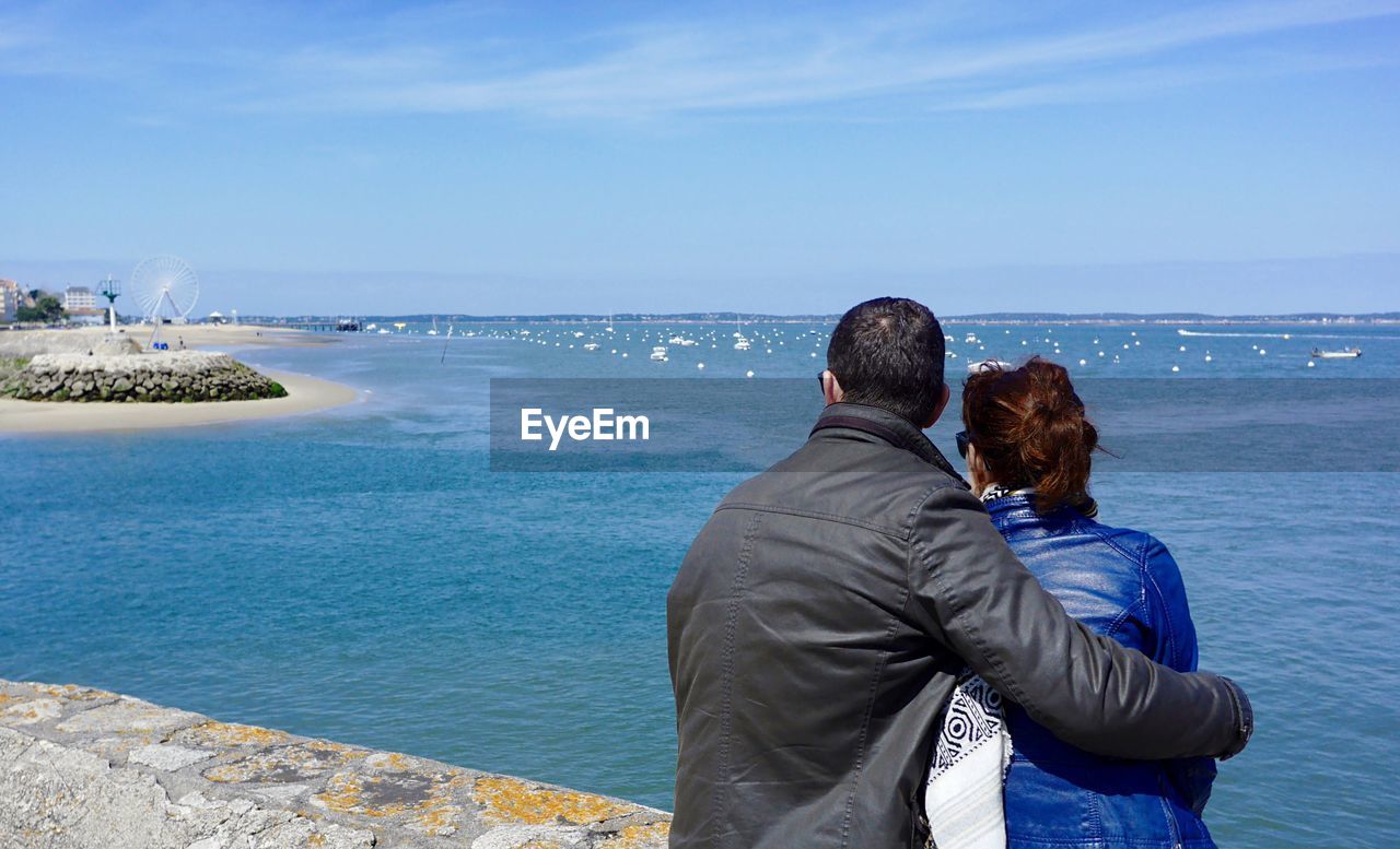 Rear view of couple overlooking calm blue sea