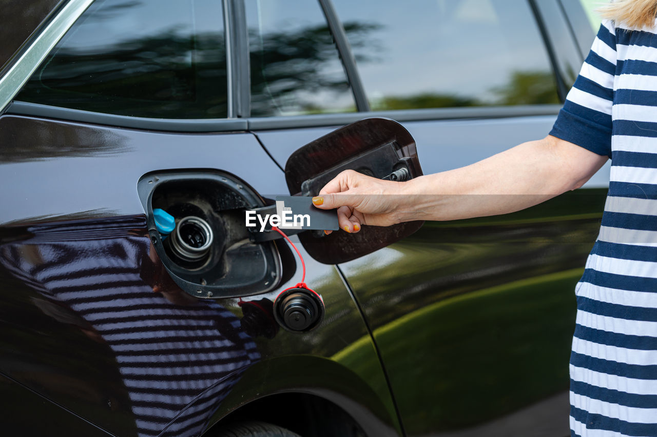 Female with credit card in front of open gas tank, fuel price rise concept, hands close-up