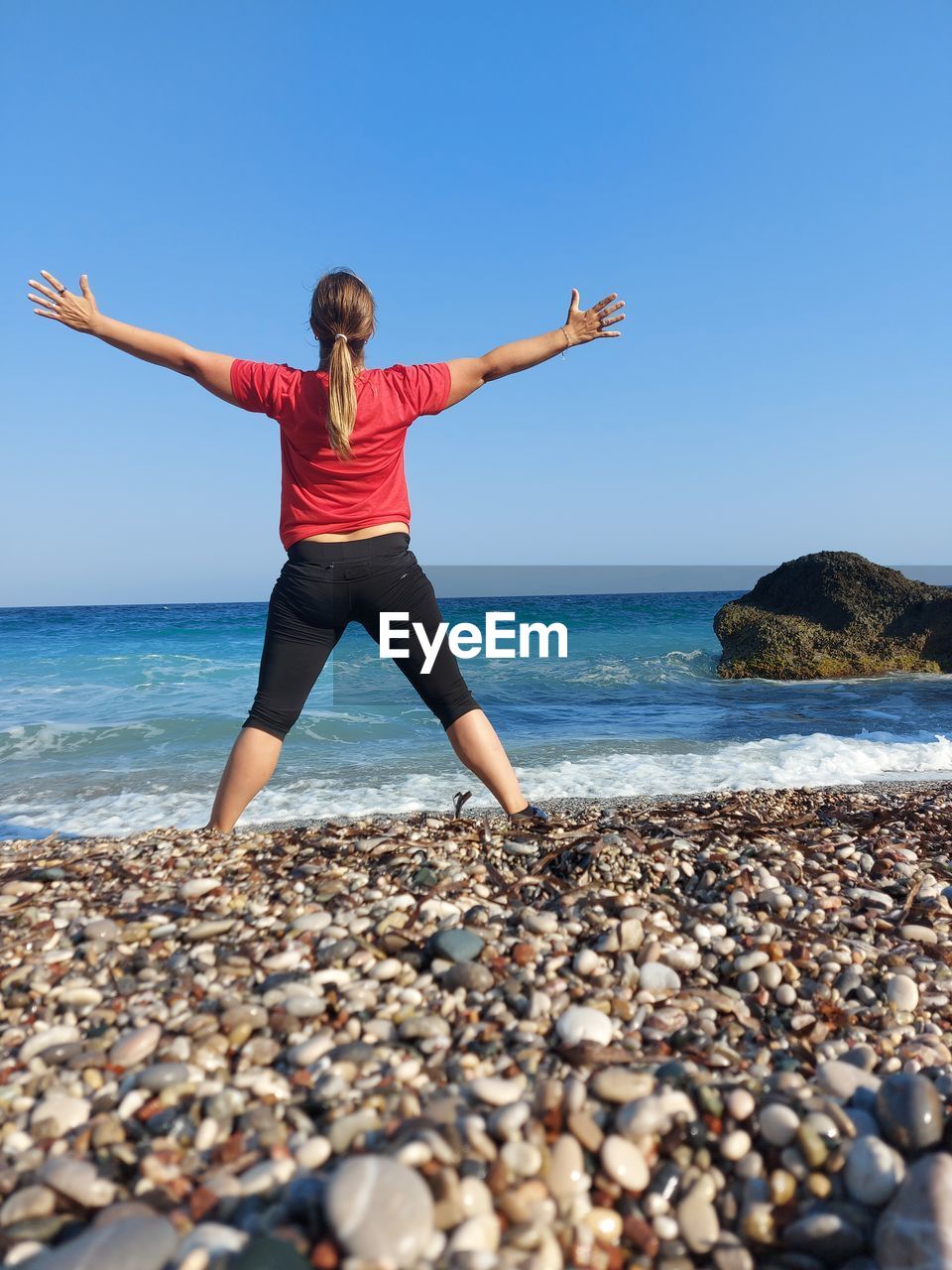 Full length of woman on rock at beach against clear sky, greece 