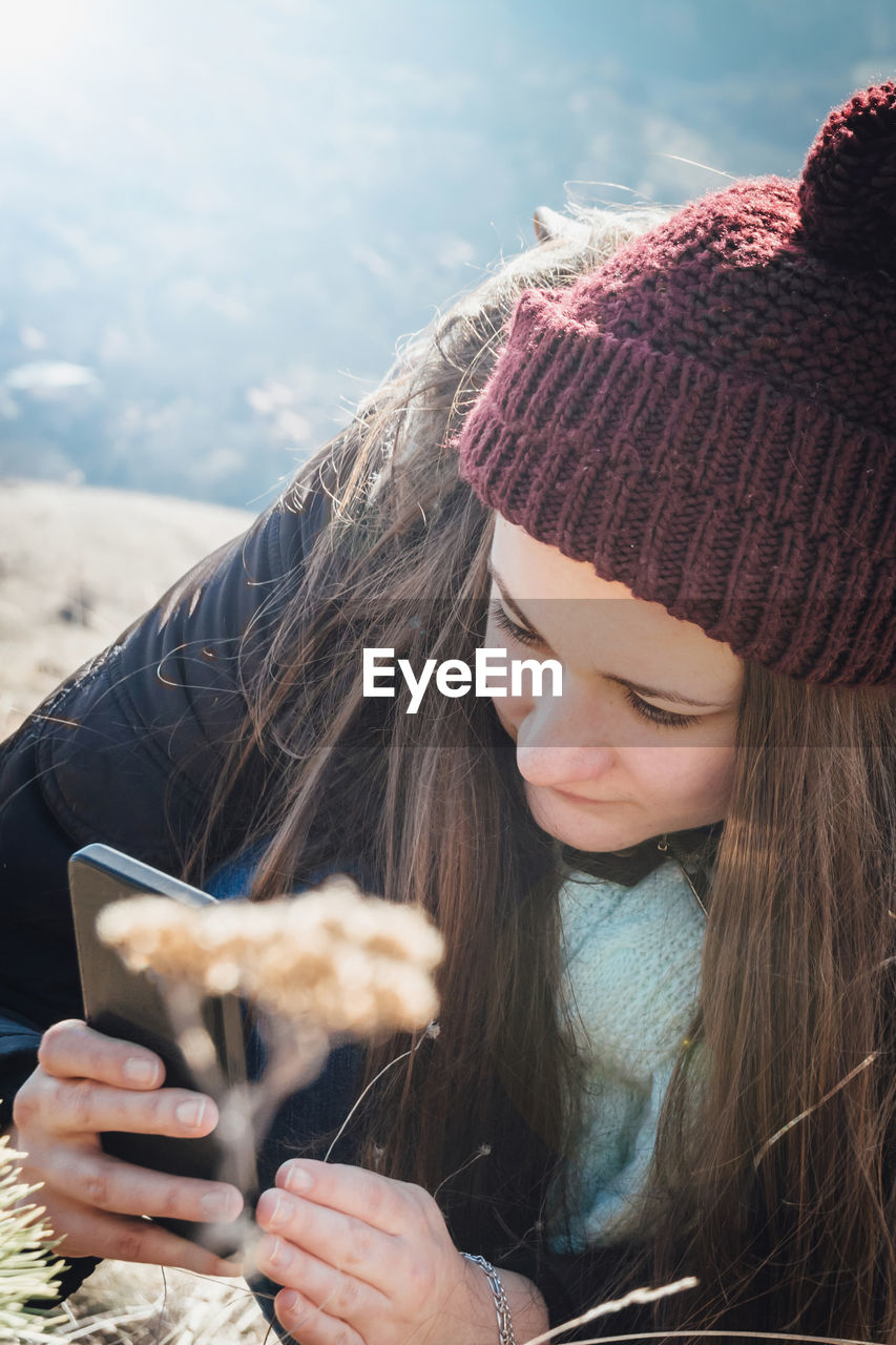 Young woman in warm clothes using mobile phone outdoors