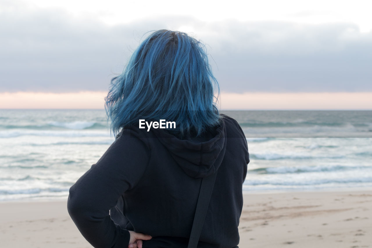 Rear view of woman standing at beach against cloudy sky