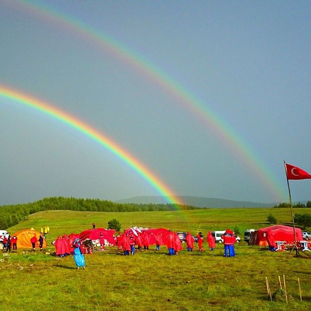 rainbow, multi colored, beauty in nature, grass, nature, sky, scenics - nature, plant, field, environment, land, double rainbow, landscape, day, idyllic, grassland, cloud, tranquility, tranquil scene, outdoors, non-urban scene, group of people, green, water, crowd, spectrum, rural scene