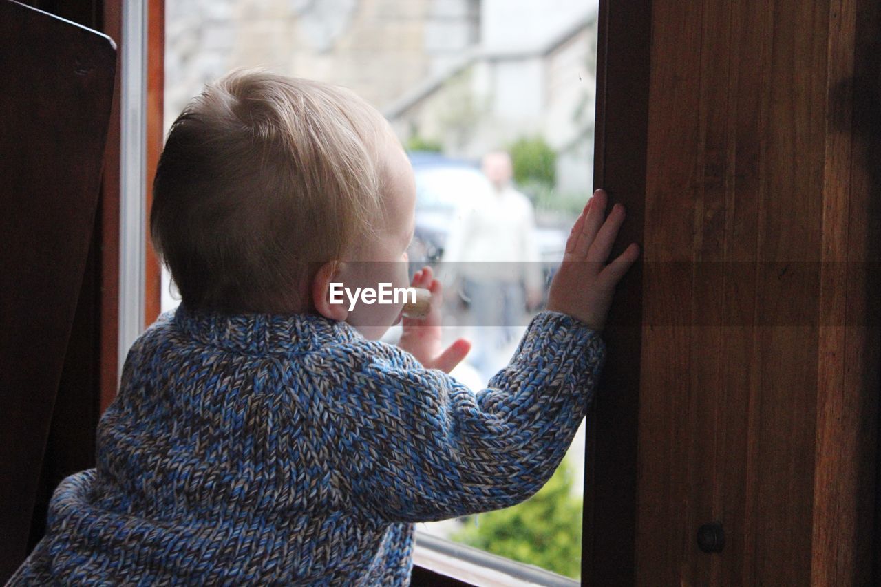 Rear view of baby boy looking through window at home