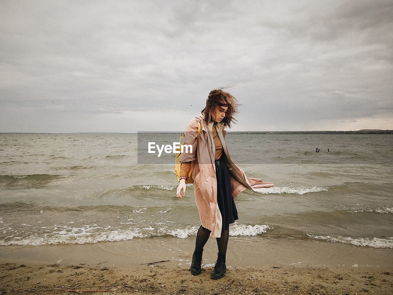 Fashionable woman standing on beach against sea against sky