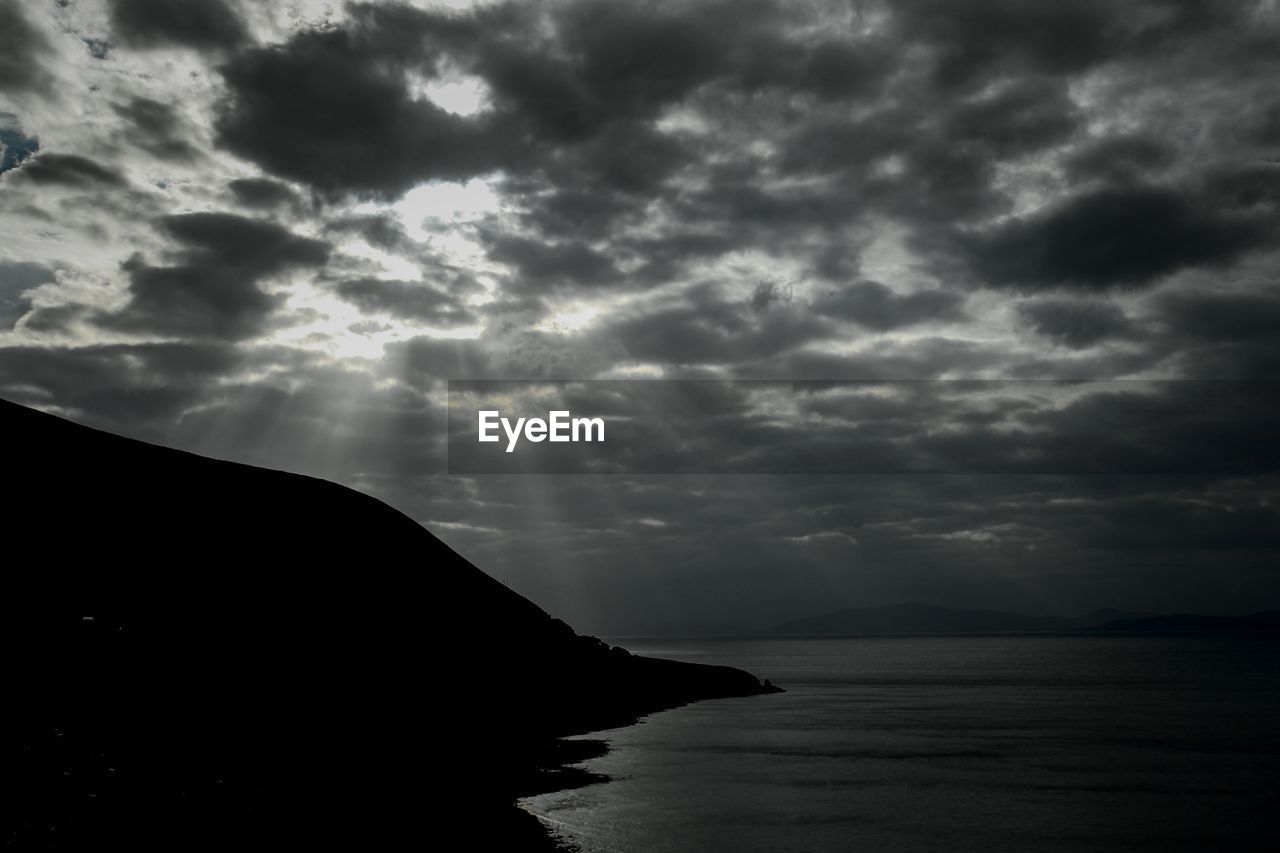 Silhouette rocky mountains and sea against cloudy sky