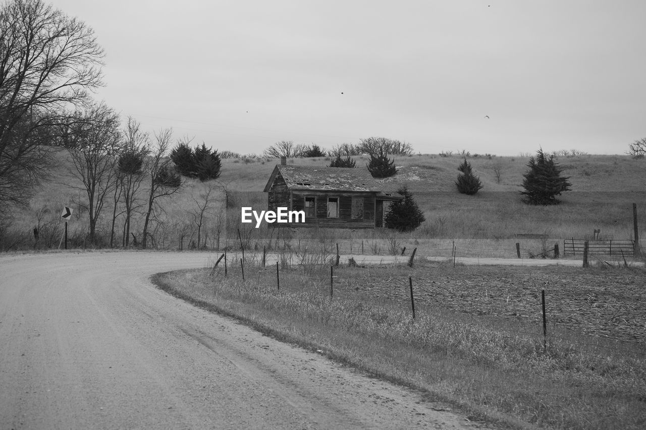 Dirt road by farm against sky