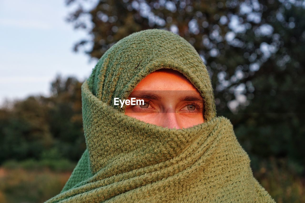 Close-up of man covering face with scarf against trees 