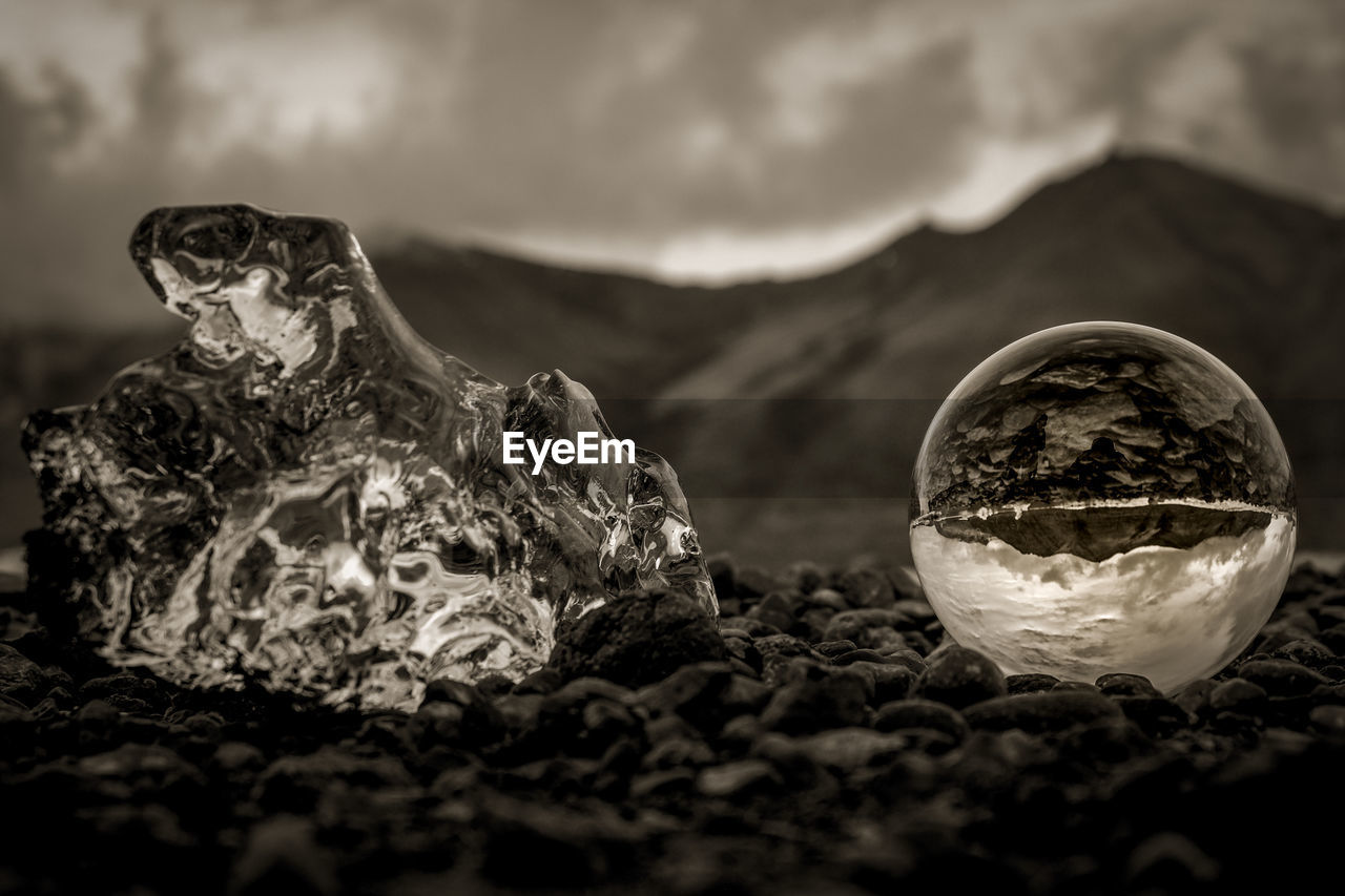 Close-up of crystal ball at beach against cloudy sky