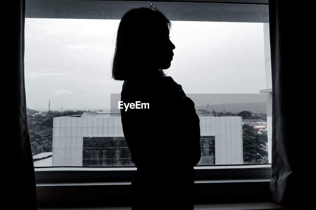 SILHOUETTE WOMAN LOOKING THROUGH WINDOW AT CITY