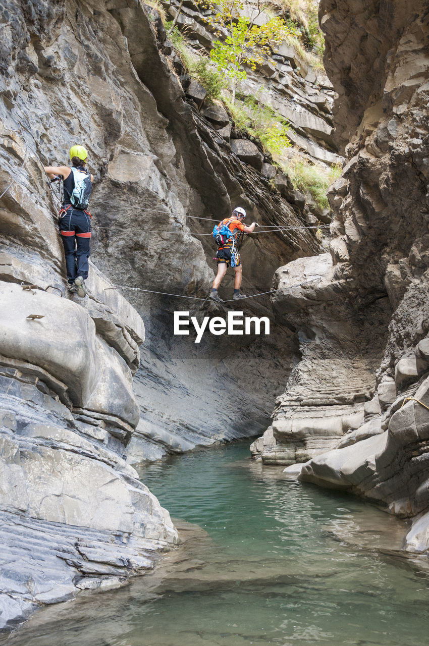 Hikers on rope over stream amidst mountains