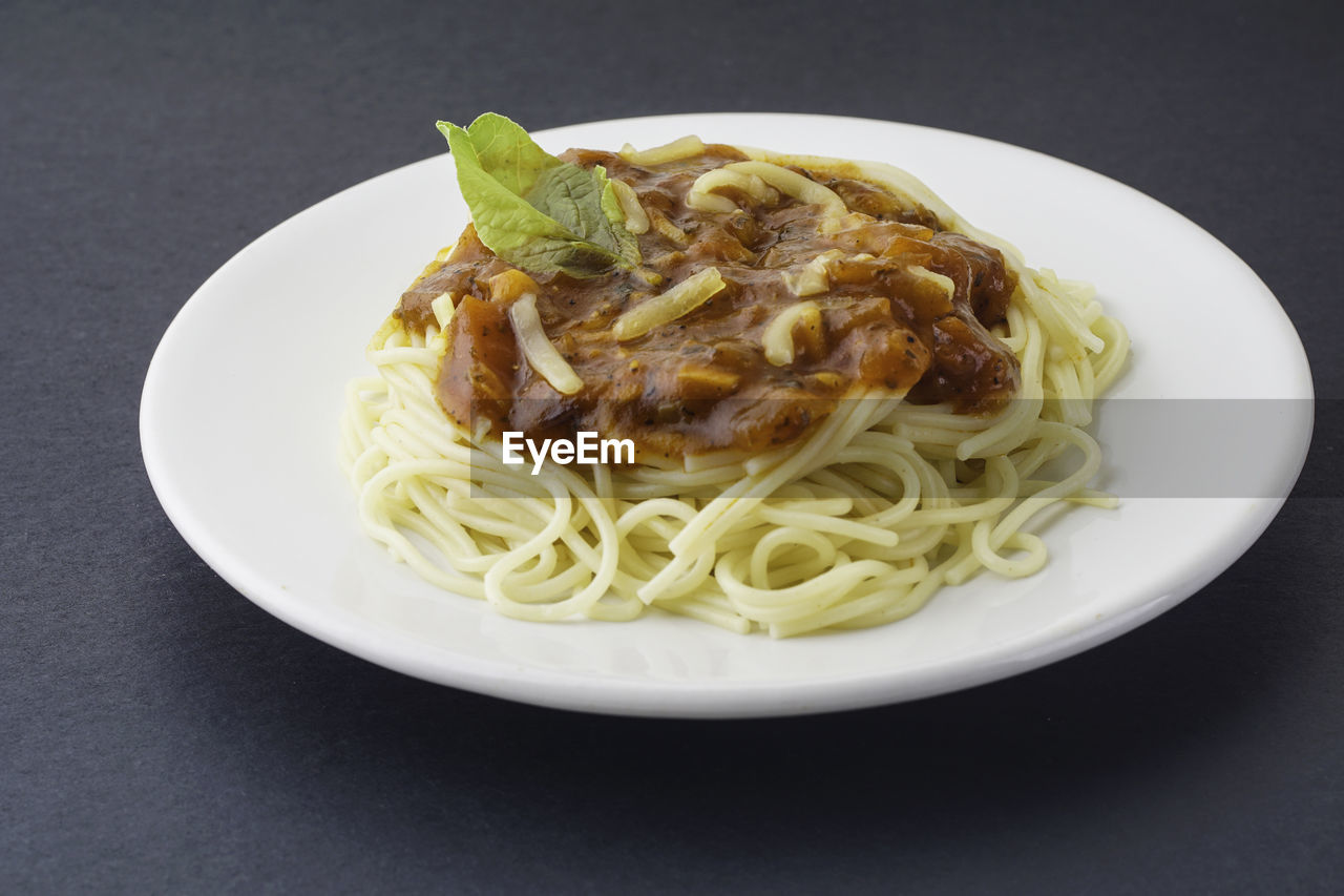 View of spaghetti bolognese with green basil on top. silver fork placed on top of the dishes.