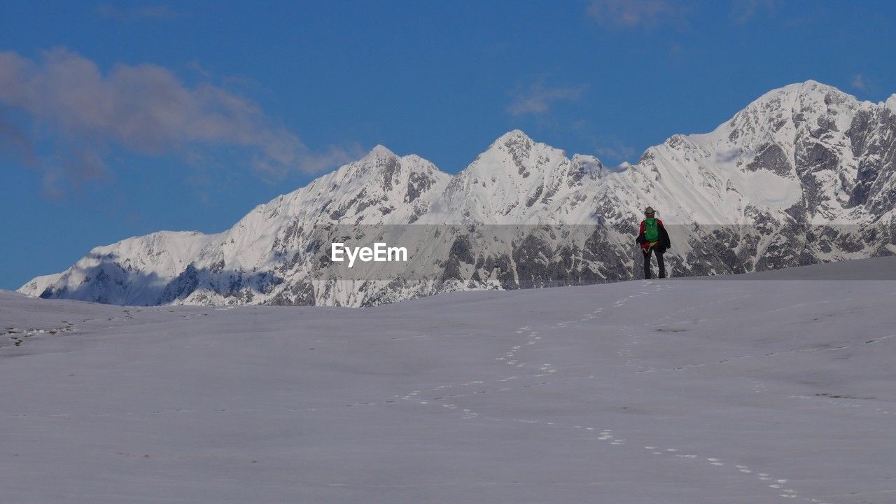 mountain, snow, winter, cold temperature, mountain range, scenics - nature, leisure activity, sky, beauty in nature, adventure, one person, sports, landscape, environment, snowcapped mountain, nature, piste, winter sports, full length, skiing, ski mountaineering, vacation, travel, holiday, ski touring, day, ridge, activity, trip, lifestyles, travel destinations, non-urban scene, cloud, hiking, land, ski equipment, ski, extreme sports, adult, tranquil scene, men, backpack, walking, outdoors, tranquility, white, tourism, summit, mountain climbing, exploration, ski holiday, recreation, tourist, blue, climbing, motion, mountaineering, rear view