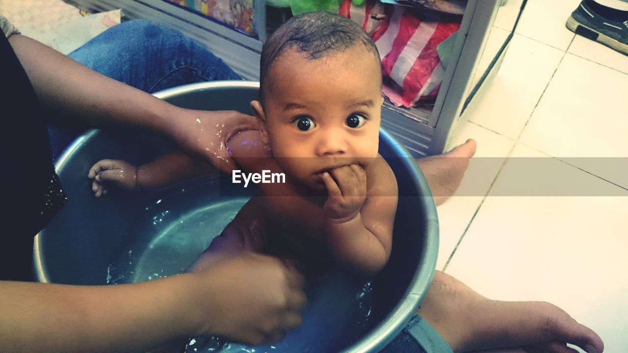 Low section of mother bathing baby boy in tub at home