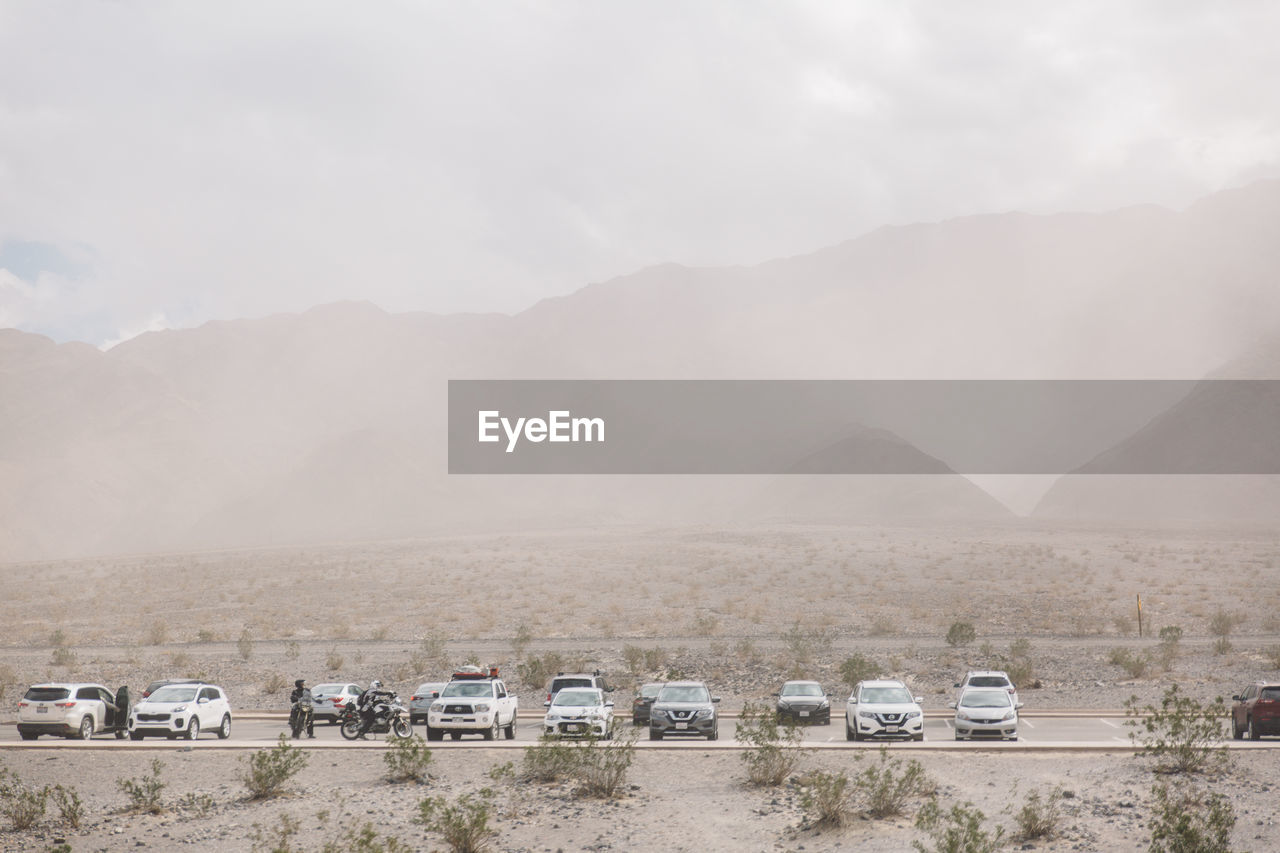 Vehicles parked at parking lot against mountains at death valley during sandstorm