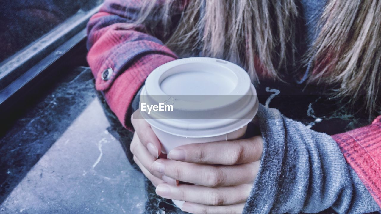 Midsection of woman holding disposable coffee cup