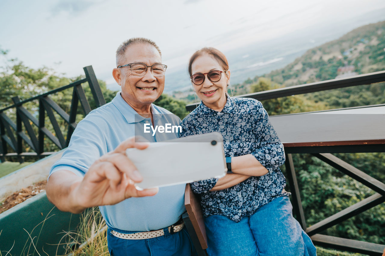 Portrait of couple taking selfie while standing by railing