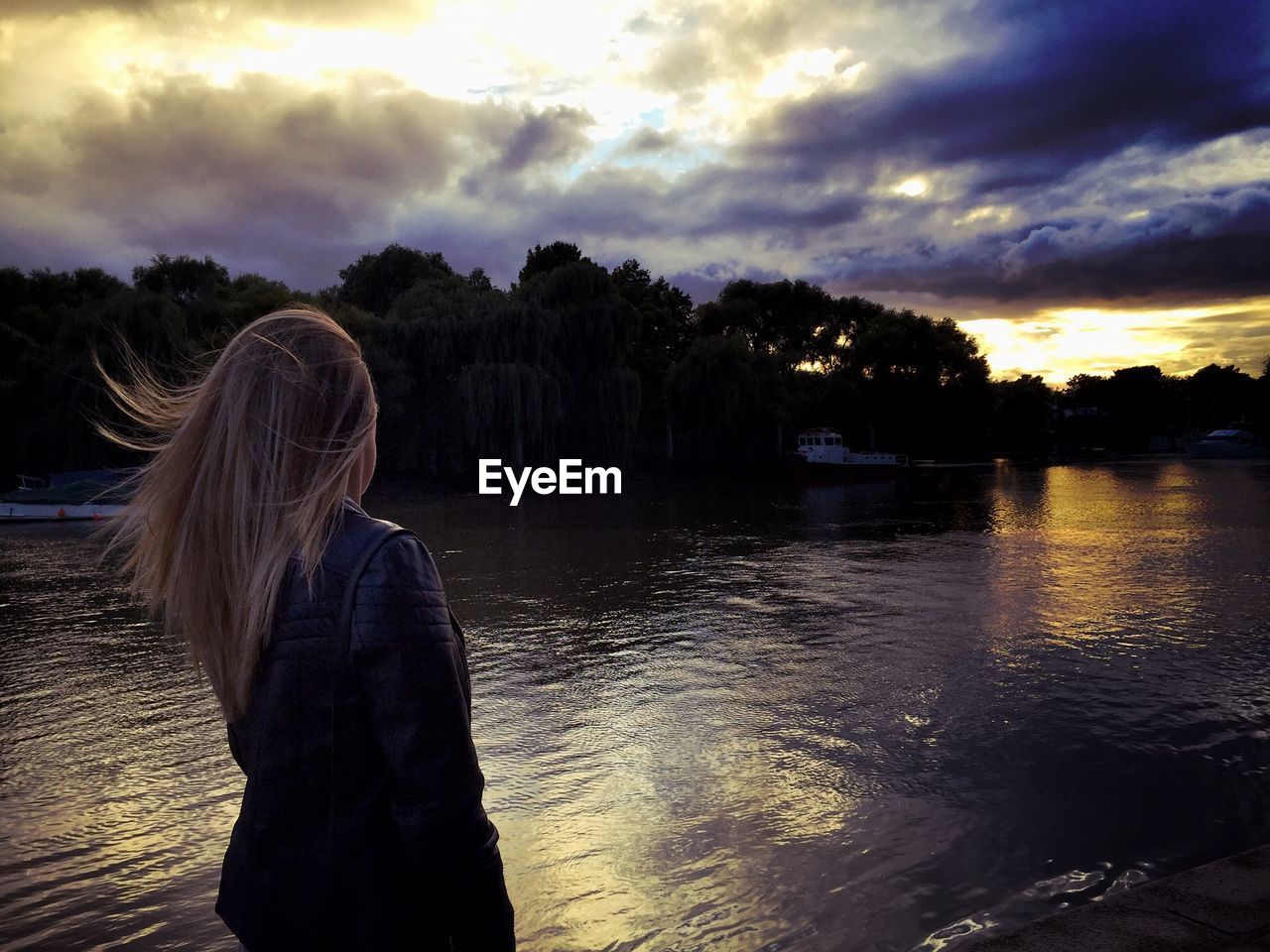 Rear view of woman standing by river during sunset