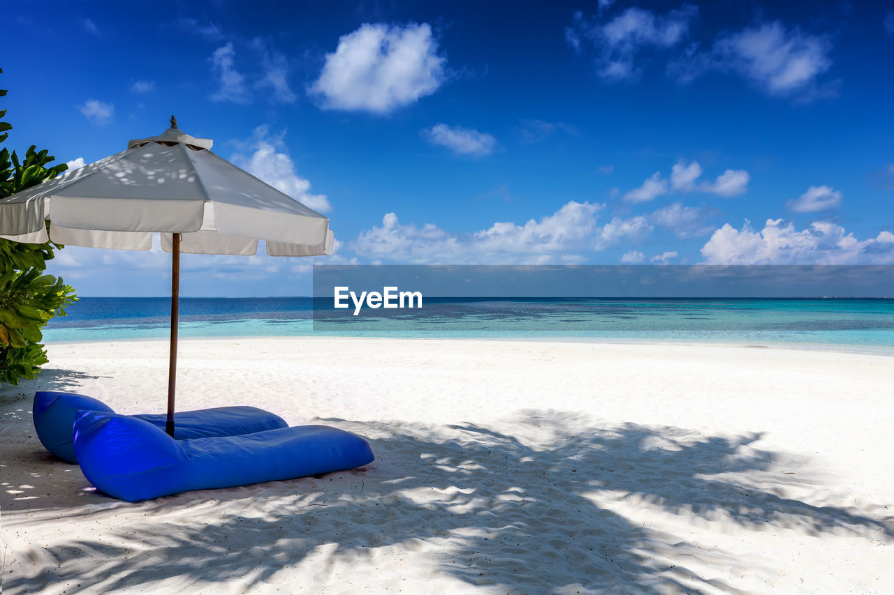 LOUNGE CHAIRS ON BEACH AGAINST BLUE SKY