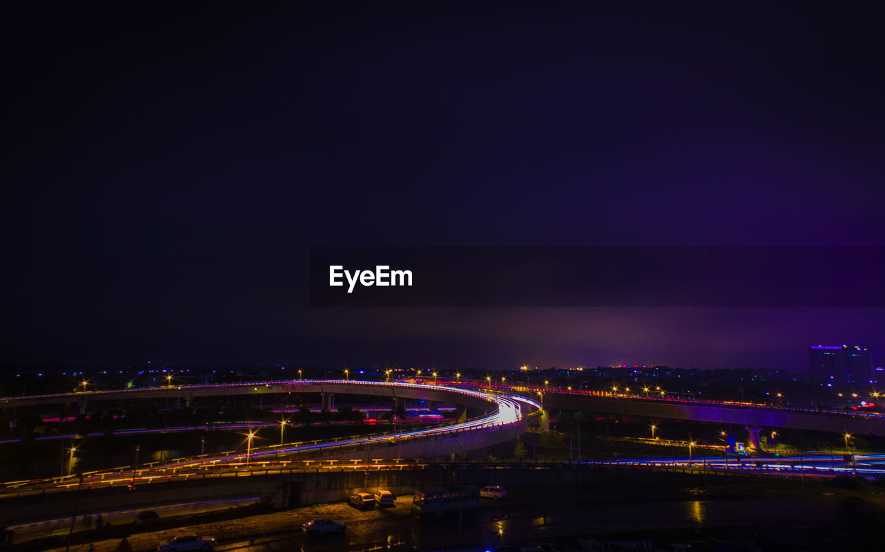 Light trails on highway in city against sky at dusk