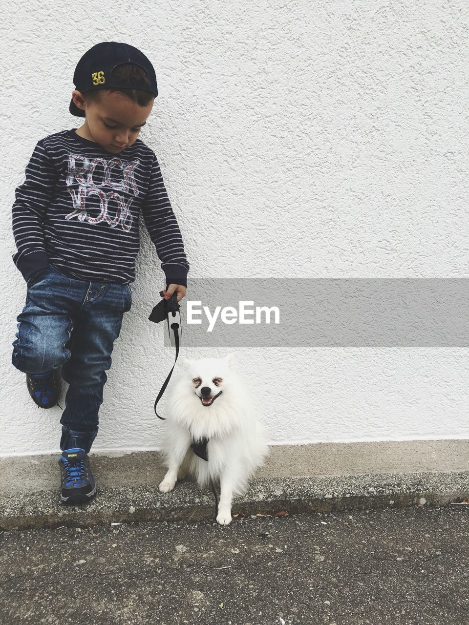 Fashionable boy standing by pomeranian against white wall