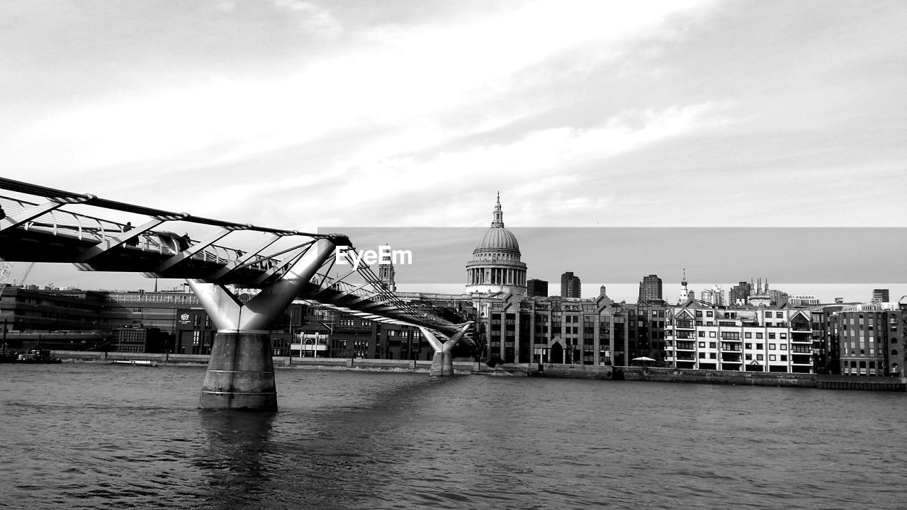 Millennium footbridge over thames river with st paul cathedral in city against sky